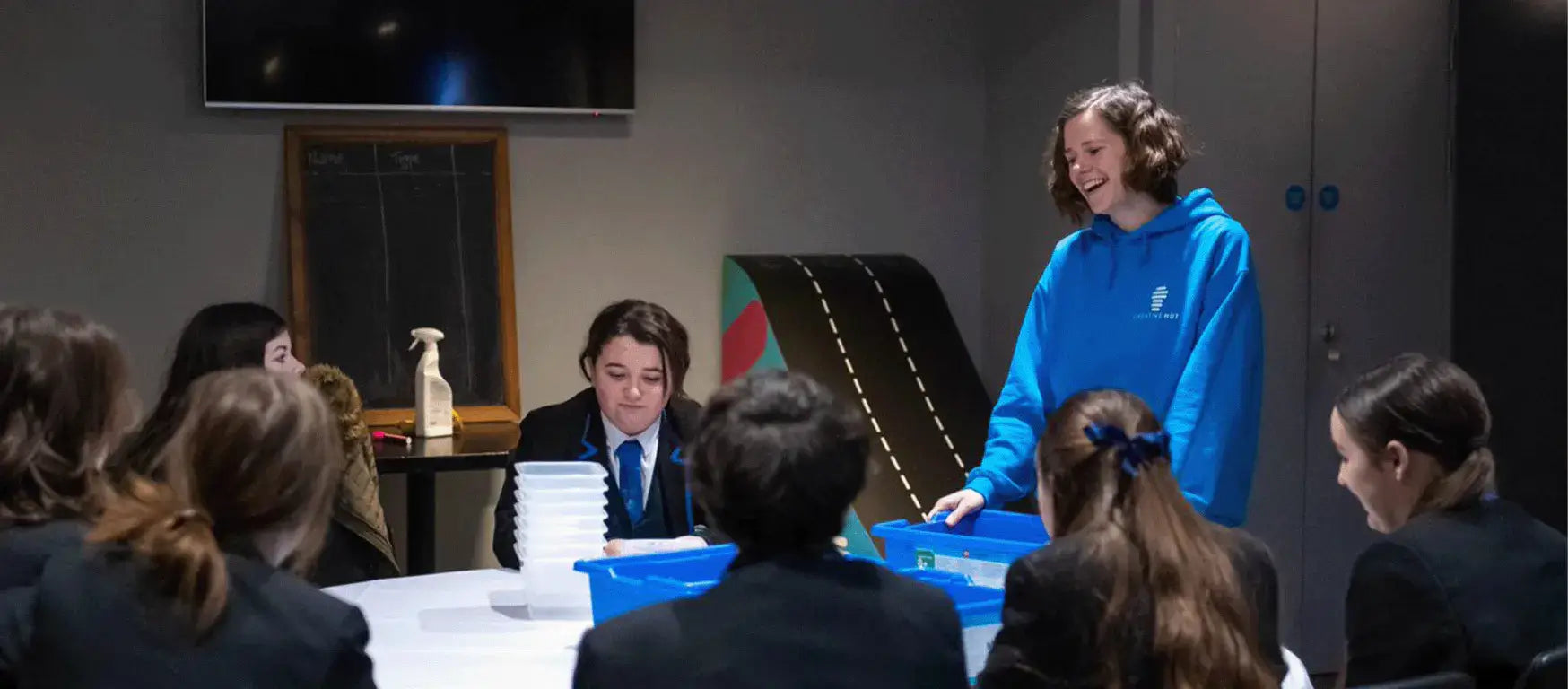 Group of students engaged in a science workshop, with a presenter in a blue hoodie leading the session.
