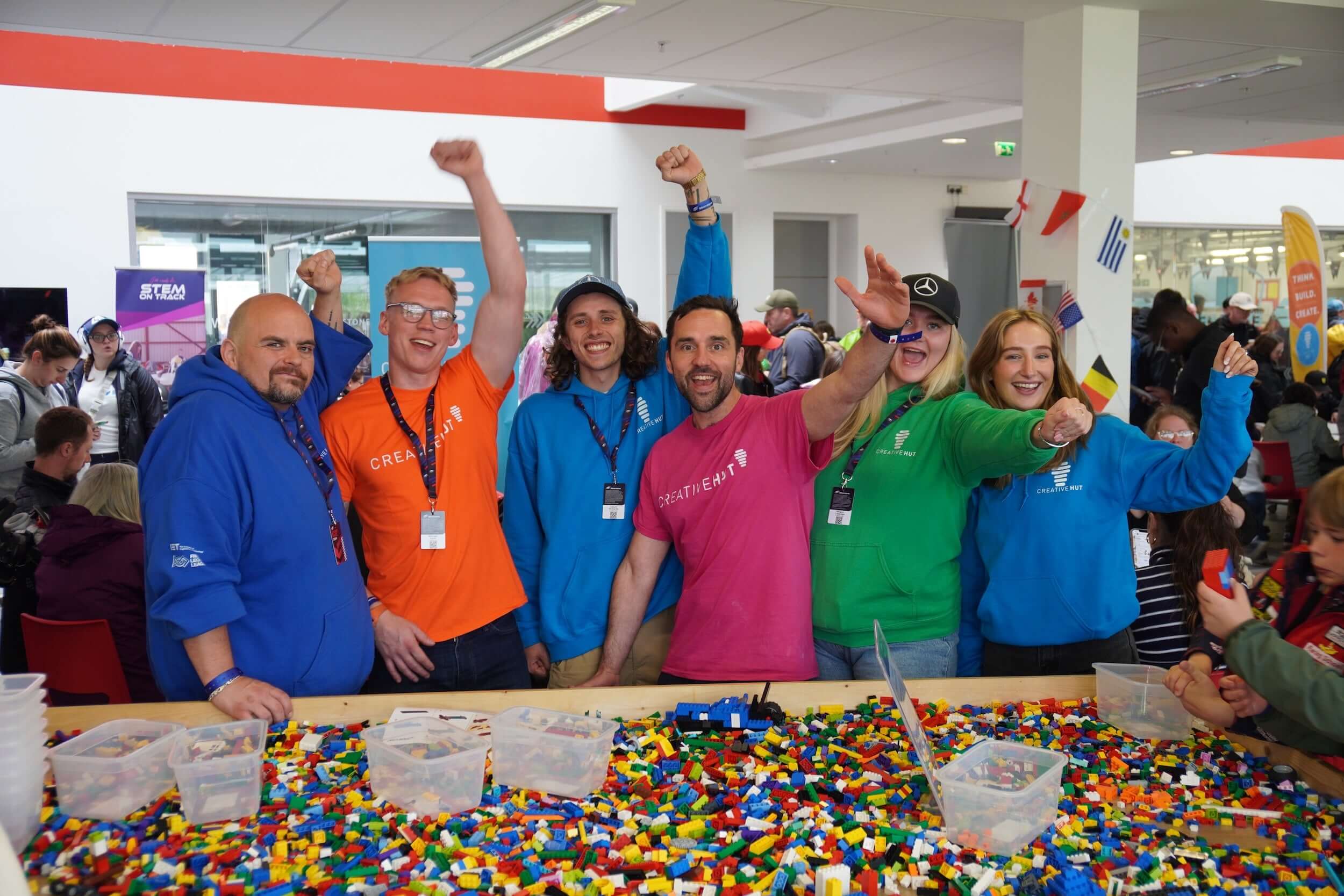 Group of enthusiastic individuals wearing colorful hoodies, celebrating at a vibrant event with LEGO bricks.