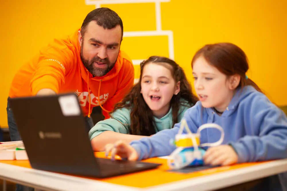 A teacher guides two excited students while they explore a laptop during a fun learning session.