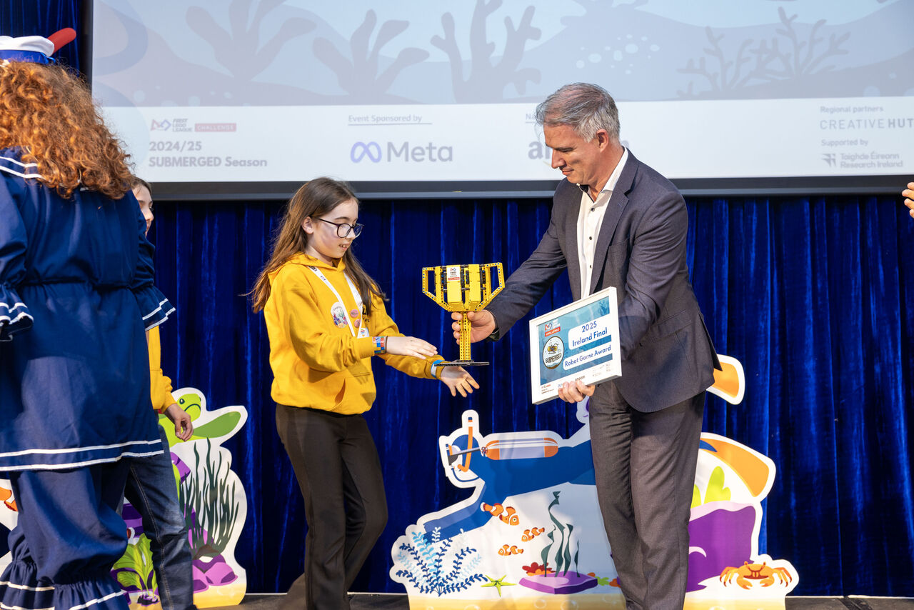 A young girl receives an award from a man at an event, surrounded by colorful marine-themed decorations.