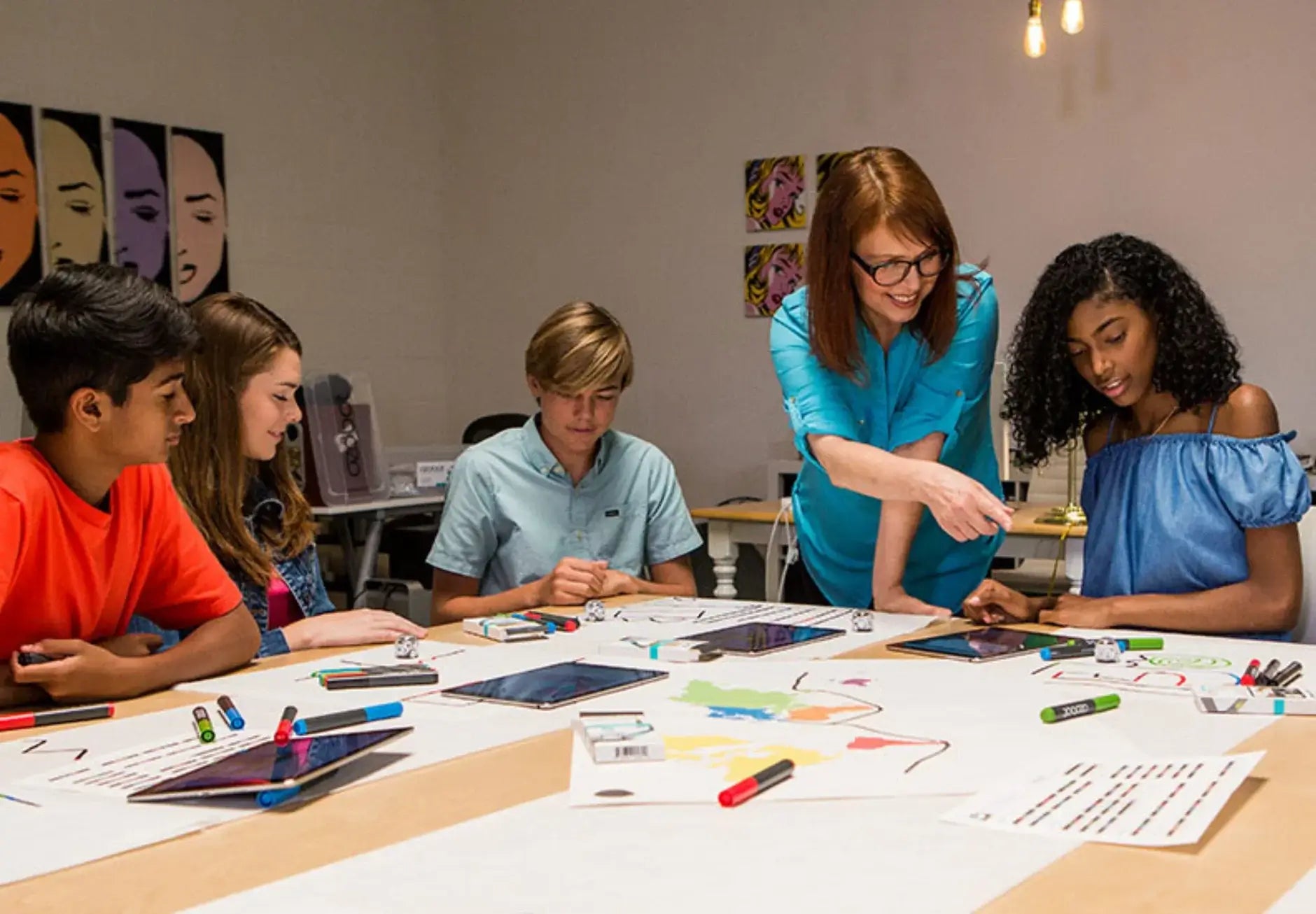Teacher guiding diverse students in an art class using tablets and markers to create colorful projects.