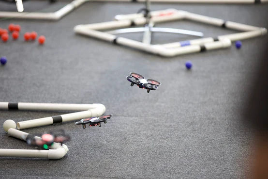 Drones flying over a competition course with obstacles made from white pipes and colored balls on the ground.