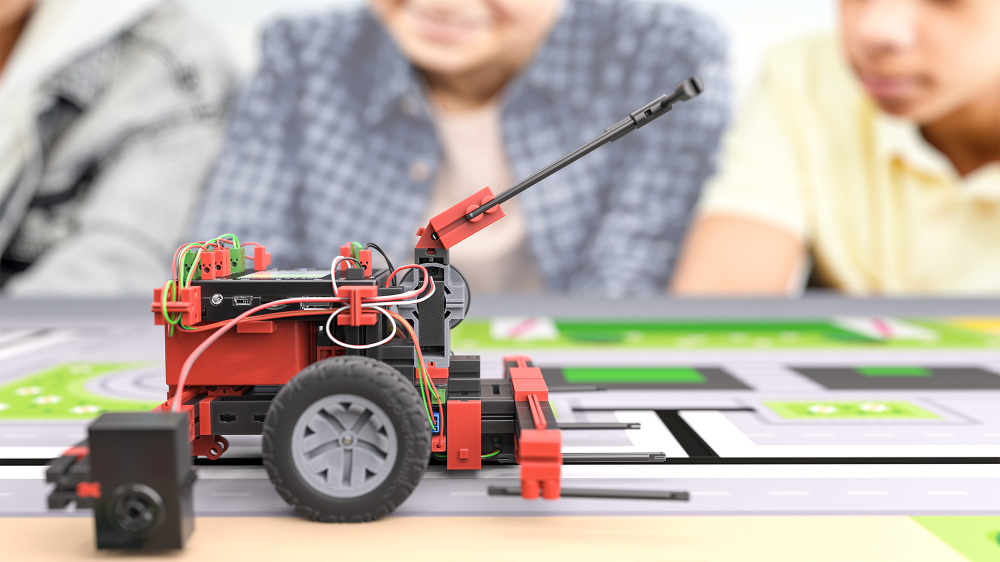 Close-up of a robotic vehicle on a track, with children collaborating in the background, showcasing STEM learning.