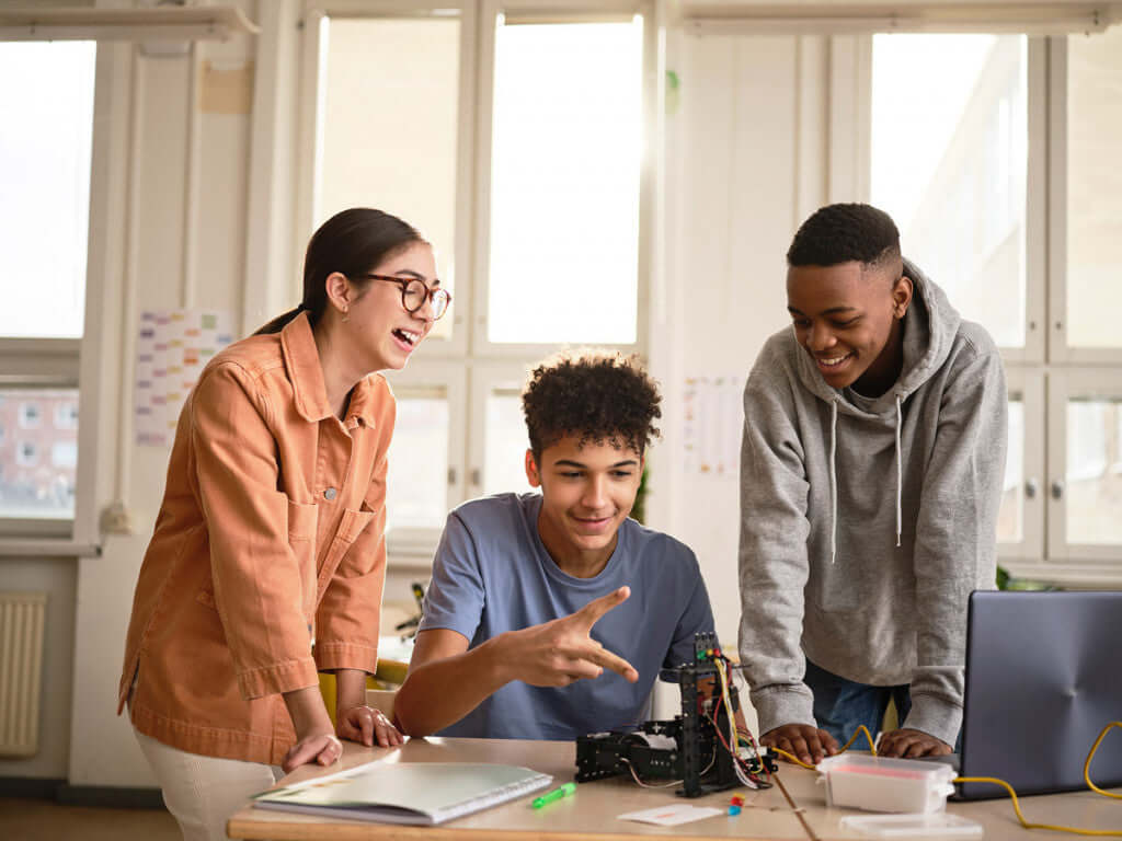 Three students collaborating on a robotics project, smiling and discussing ideas during a creative learning session.