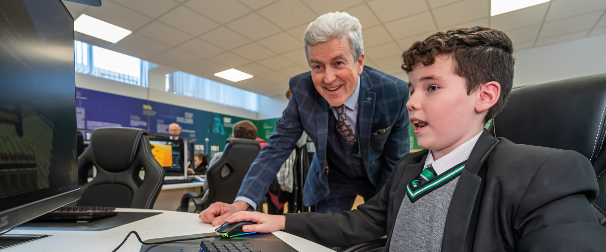 Teacher assisting a student at a computer in a modern classroom, promoting hands-on learning and engagement in technology.