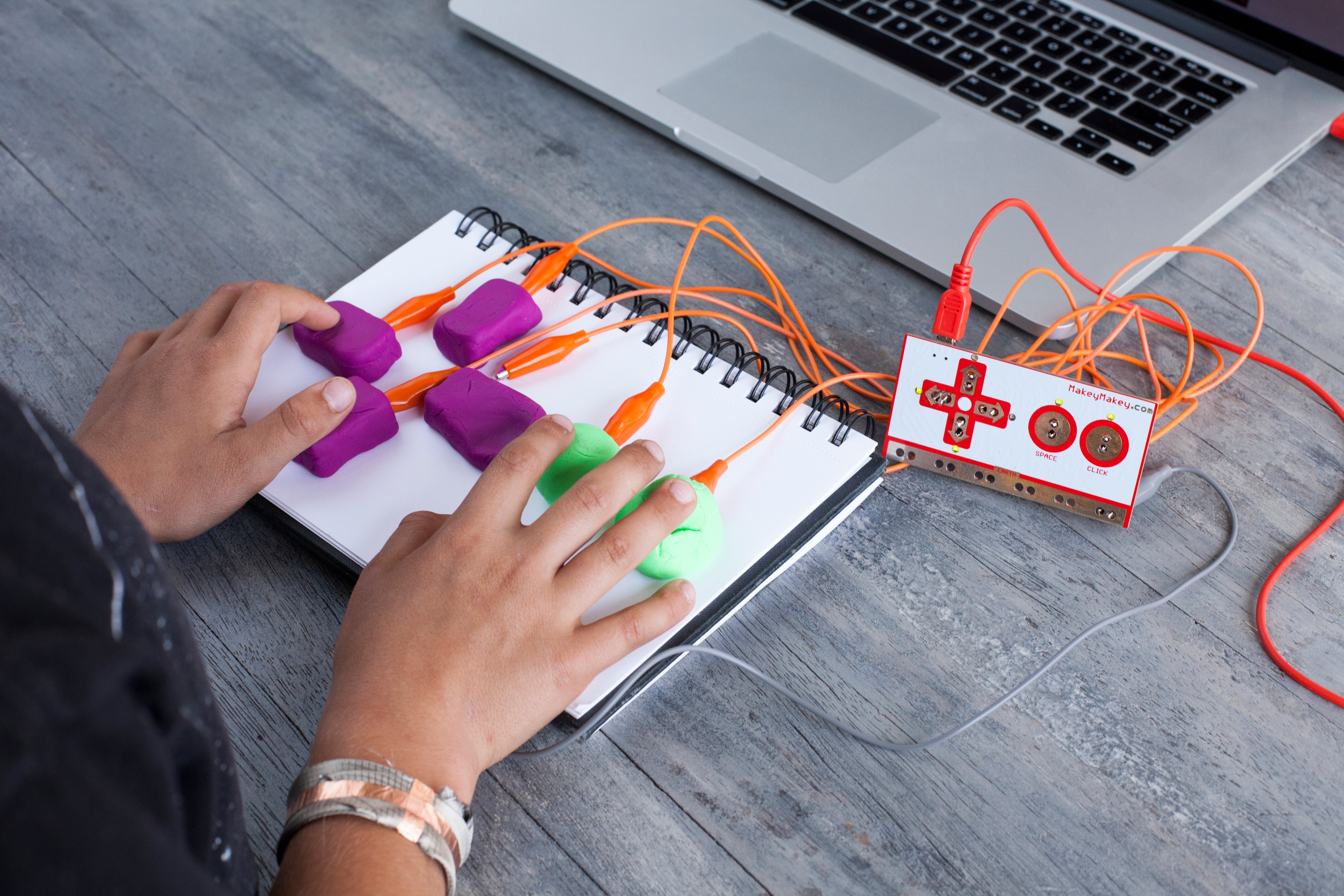 Hands using interactive tech on a notebook with colorful buttons and a laptop in a modern workspace.