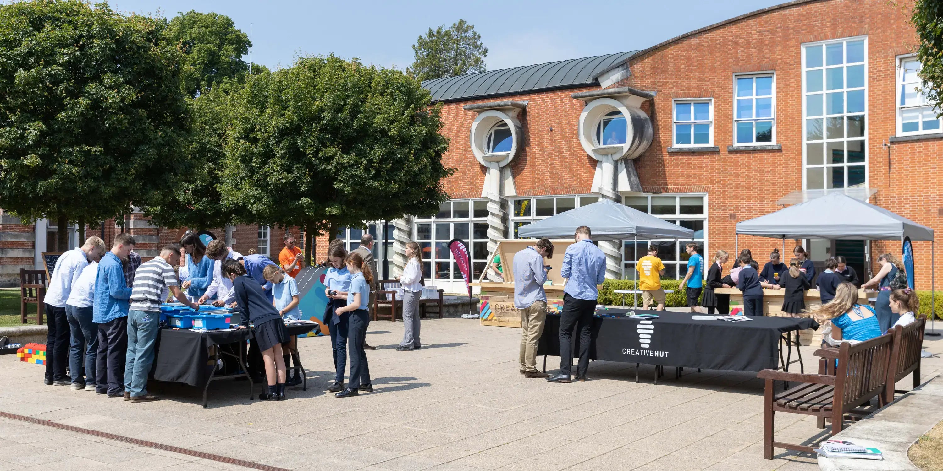 People gathered at outdoor event with tents and activities in a sunny courtyard setting.