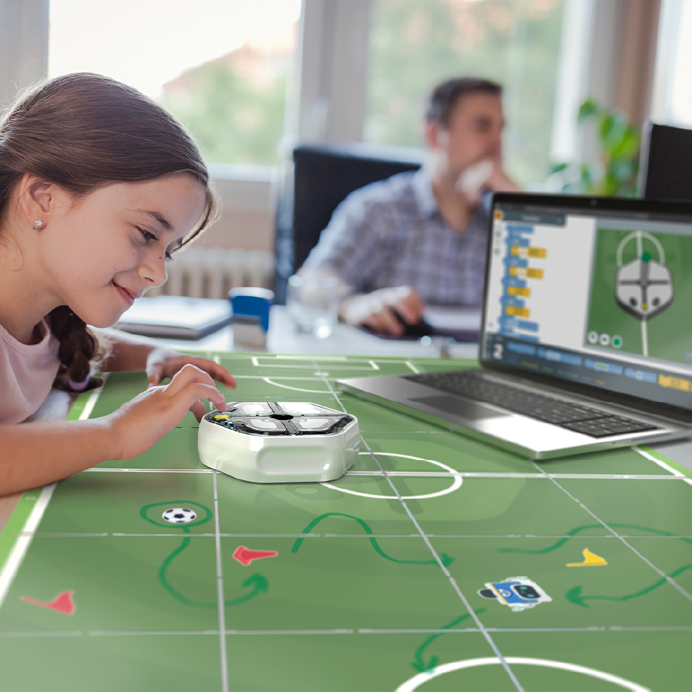 Young girl engaged in coding a soccer robot on a digital game board with a laptop in a bright workspace.