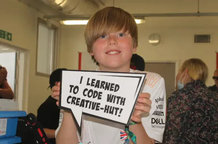 A young boy holds a sign that says 'I learned to code with Creative-Hut' at a coding workshop.