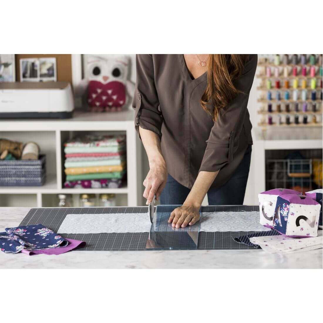 Woman using Cricut Self-Healing Cutting Mat to cut fabric with colorful patterned materials and sewing supplies nearby.