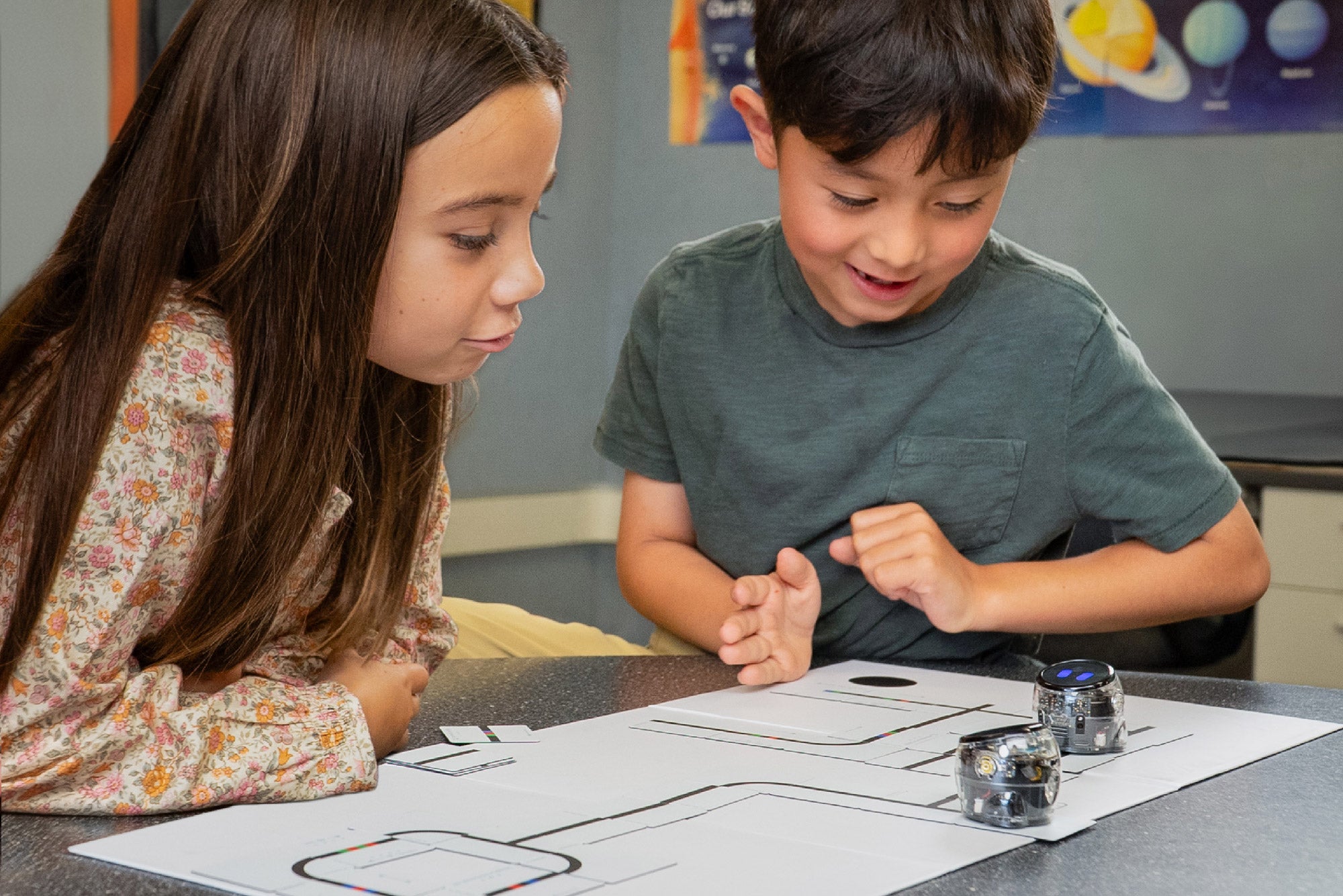 Two children engaged in hands-on learning with robots on a printed maze, showcasing teamwork and STEM education.