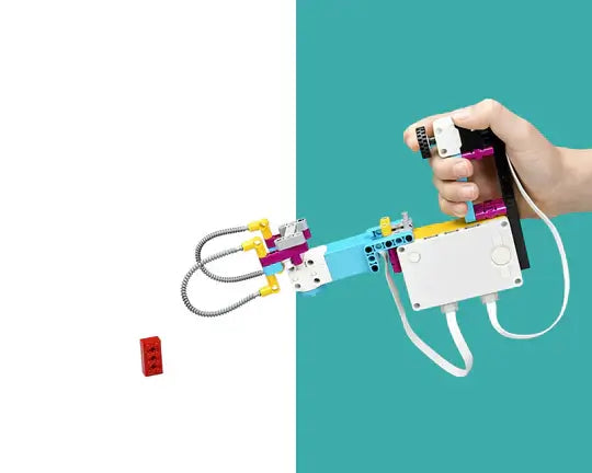 A hand holding a colorful robotic arm made of building blocks, aiming at a small red block.
