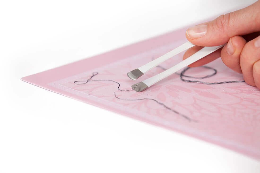 Cricut applicator set with tweezers removing fabric threads from Cricut FabricGrip mat.