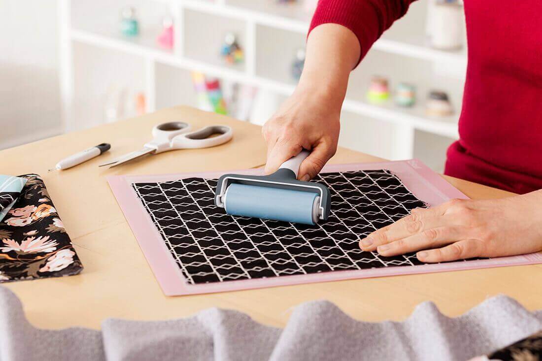 Person using Cricut applicator roller on fabric mat for seamless application in sewing projects.