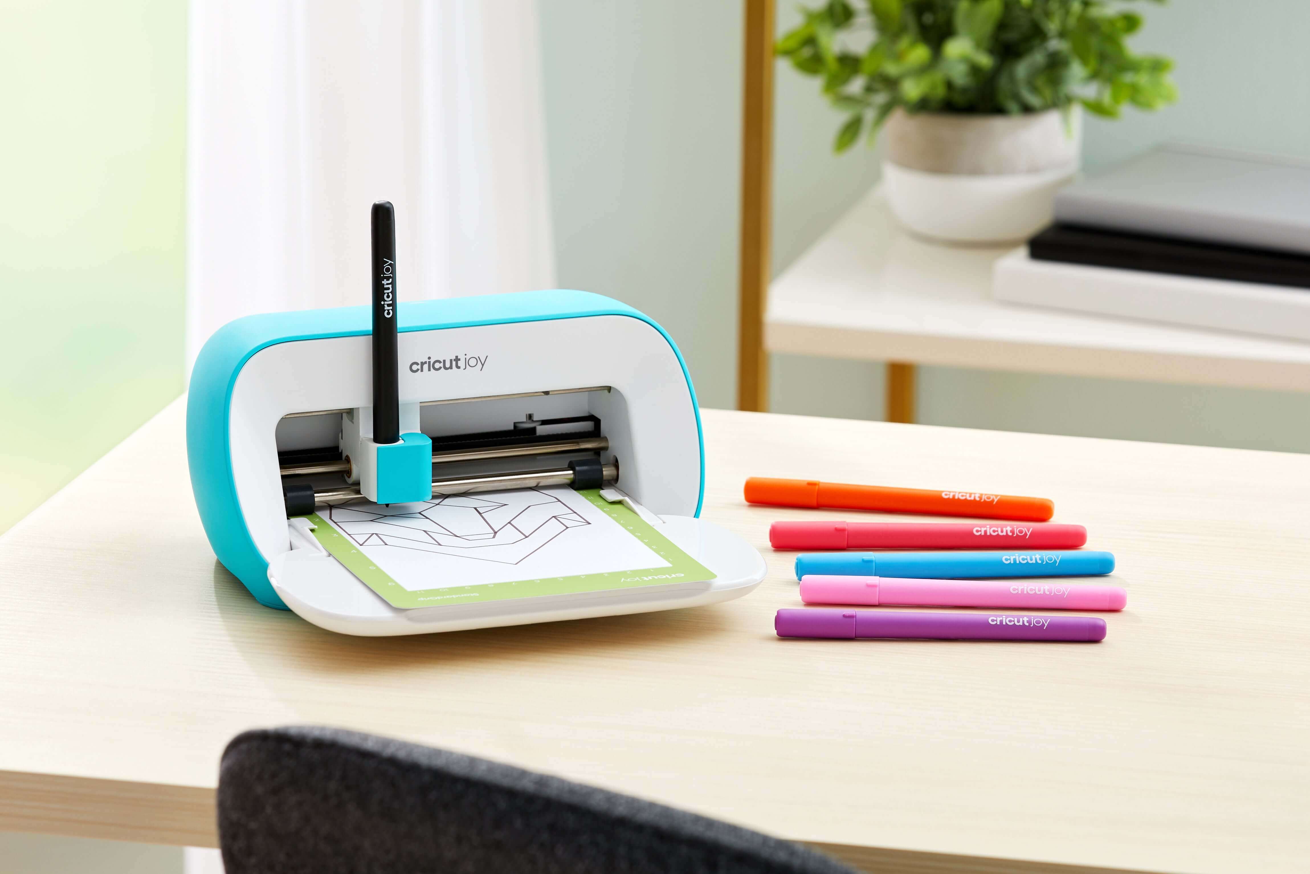 Cricut Joy cutting machine on a table with colorful markers for DIY projects and personalization.