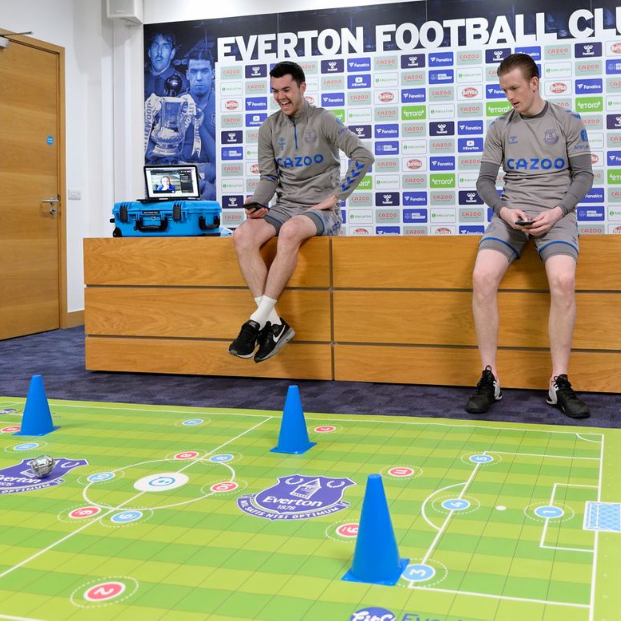Two athletes sitting by an Everton Football Club backdrop, interacting with a football-themed coding mat.