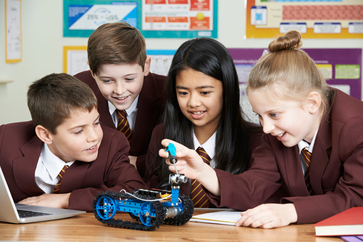 Students engaging with a robotics project, examining a blue robotic car while using a laptop in a classroom setting.