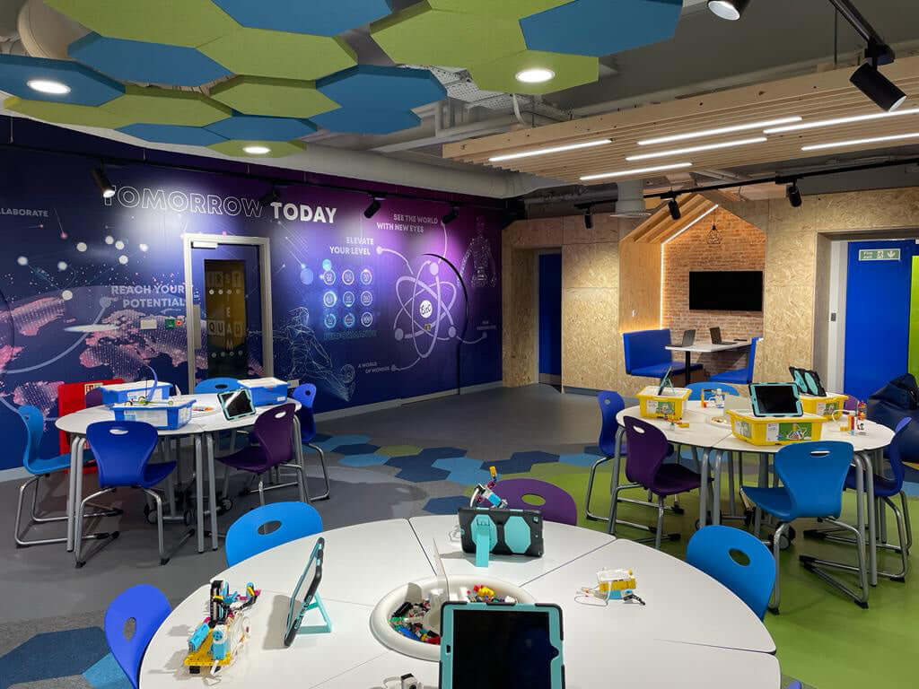 Bright educational space with colorful tables, tech setup, and inspiring wall art promoting creativity and innovation.