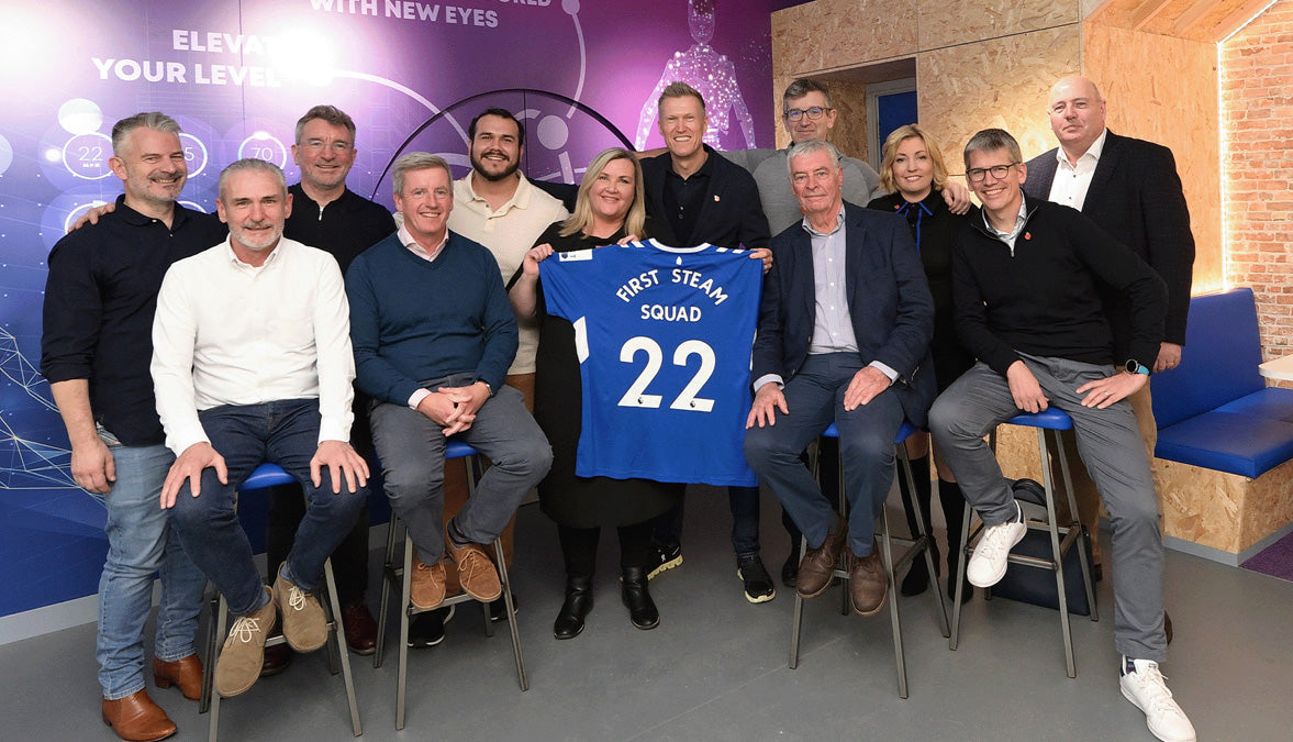Group photo of a sports team with members holding a blue jersey labeled 'First Team Squad 22' in a modern setting.