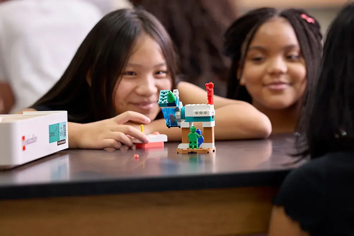 Two girls engaged in building with a colorful LEGO creation, showcasing creativity in a classroom setting.