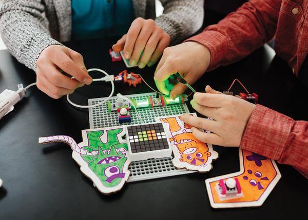 Hands assembling the littleBits Code Kit with colorful creations and interactive electronics on a workspace.