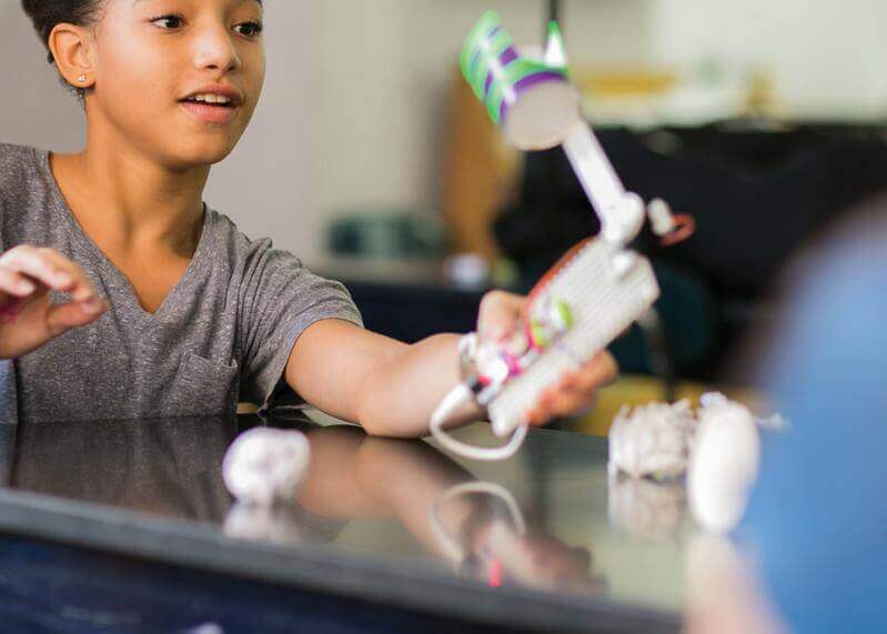 A child excitedly demonstrates a creative invention made with littleBits in a classroom setting.