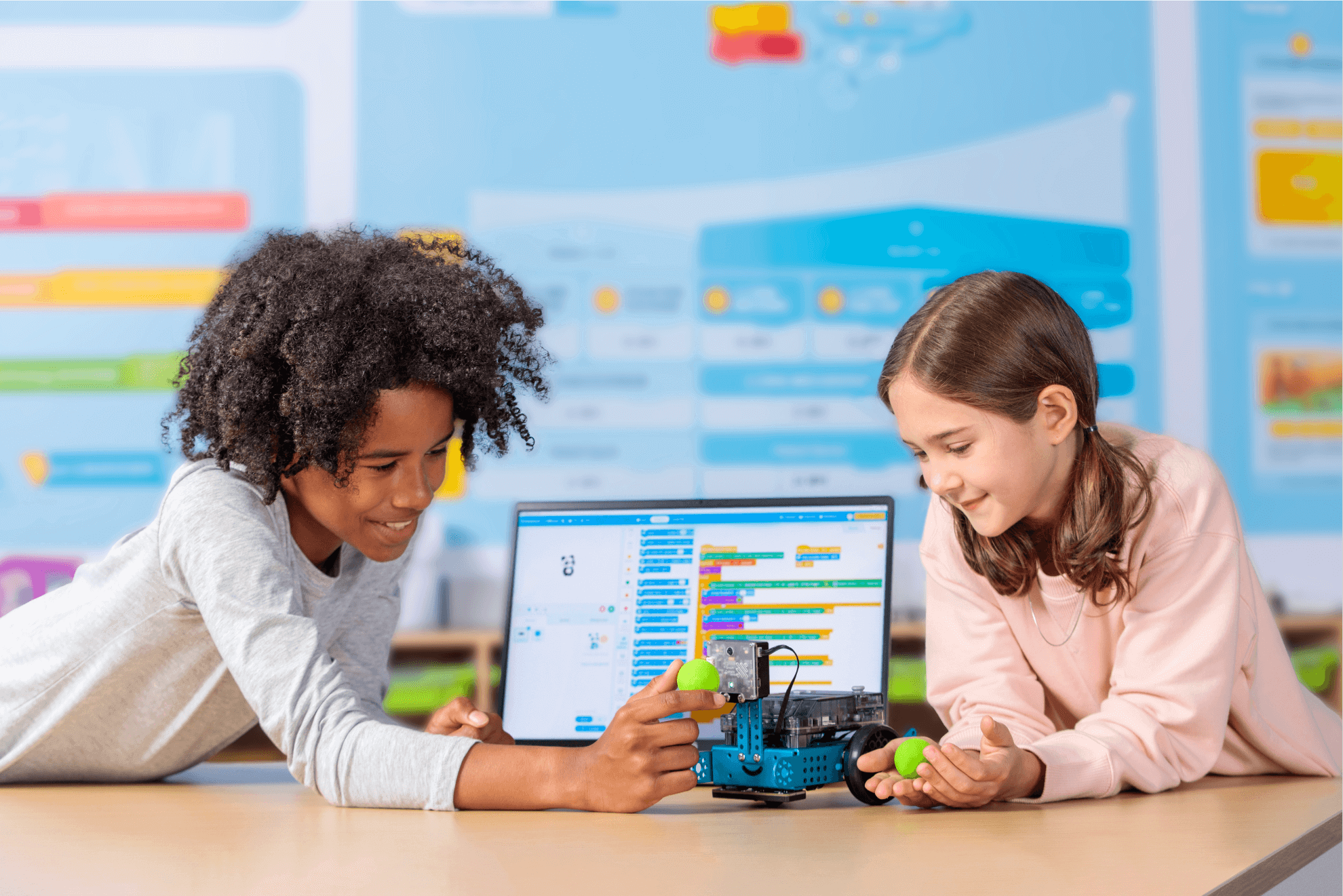 Two children engaging with the Makeblock mBot 2 robot while programming on a laptop.