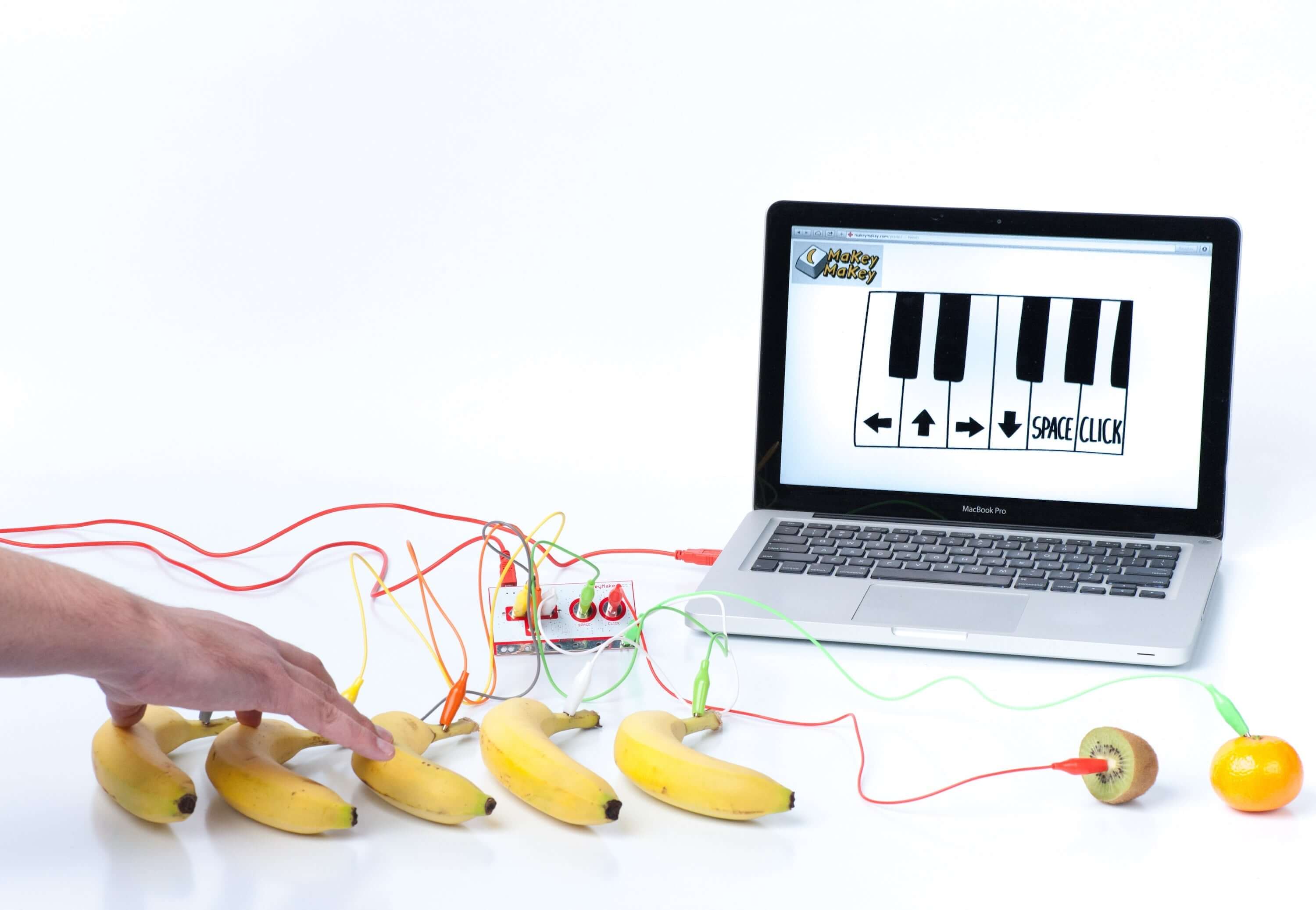 A hand using bananas as piano keys connected to a laptop running a music program with Makey Makey®.