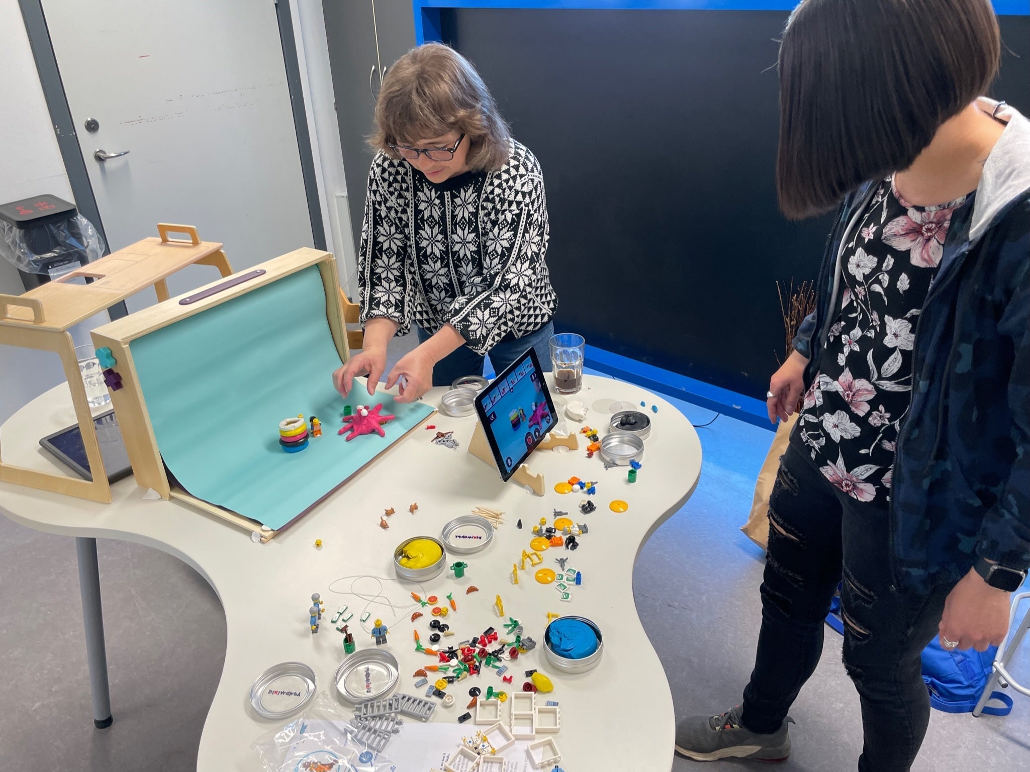 Two people using Piximakey Animation Studio to create stop motion scenes with colorful props and a tablet.