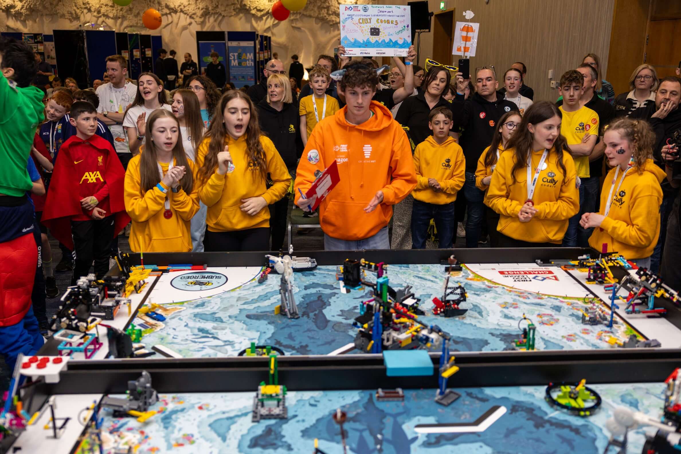 Excited participants in yellow hoodies engage in a robotics competition at a vibrant event.