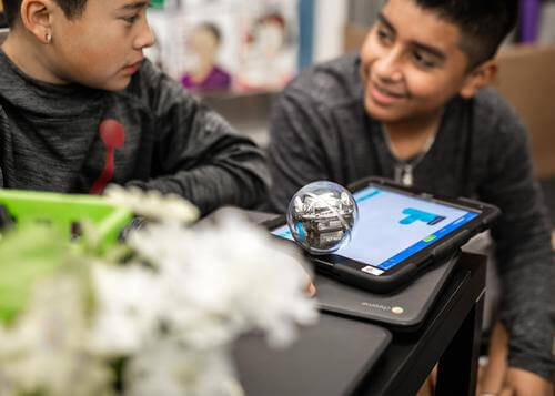 Two students engaging with a Sphero robot on a tablet, exploring computer science principles in the classroom.