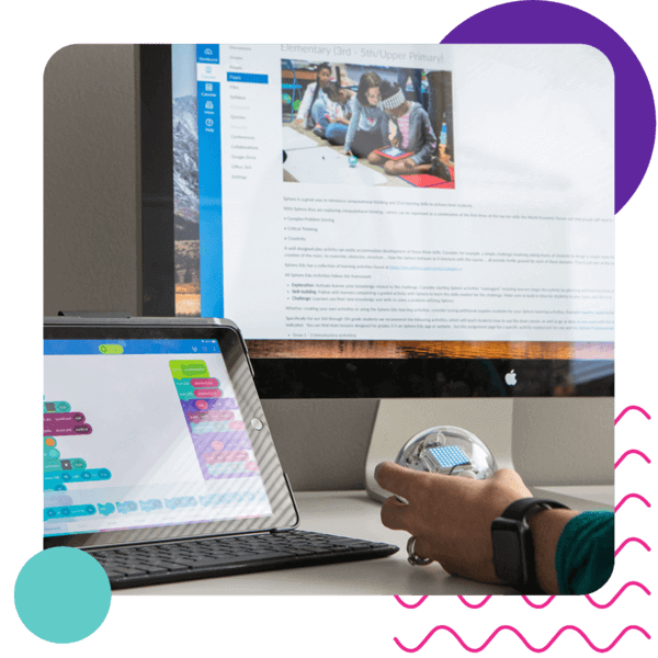 A person programming on a tablet while interacting with a Sphero robot, showcasing an educational tech setup.