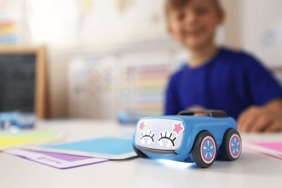 Sphero indi classroom pack robot on a table with colorful learning cards and a smiling child in the background.