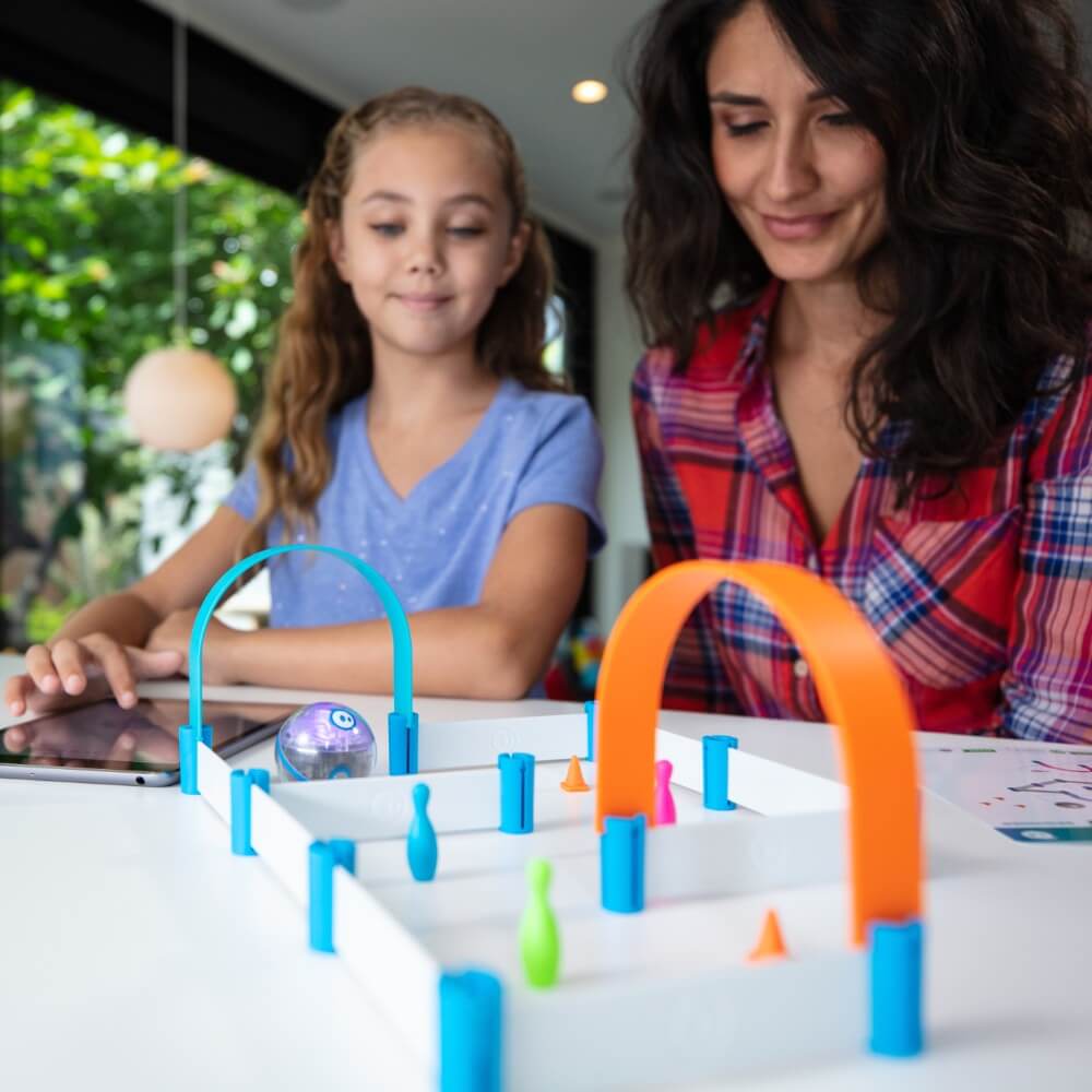 A mother and daughter enjoying a colorful tabletop game featuring a small robot and various obstacles.