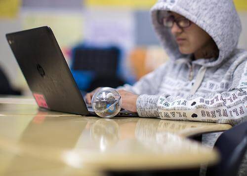 Student programming with Sphero robot on laptop in a classroom setting, enhancing computer science skills.