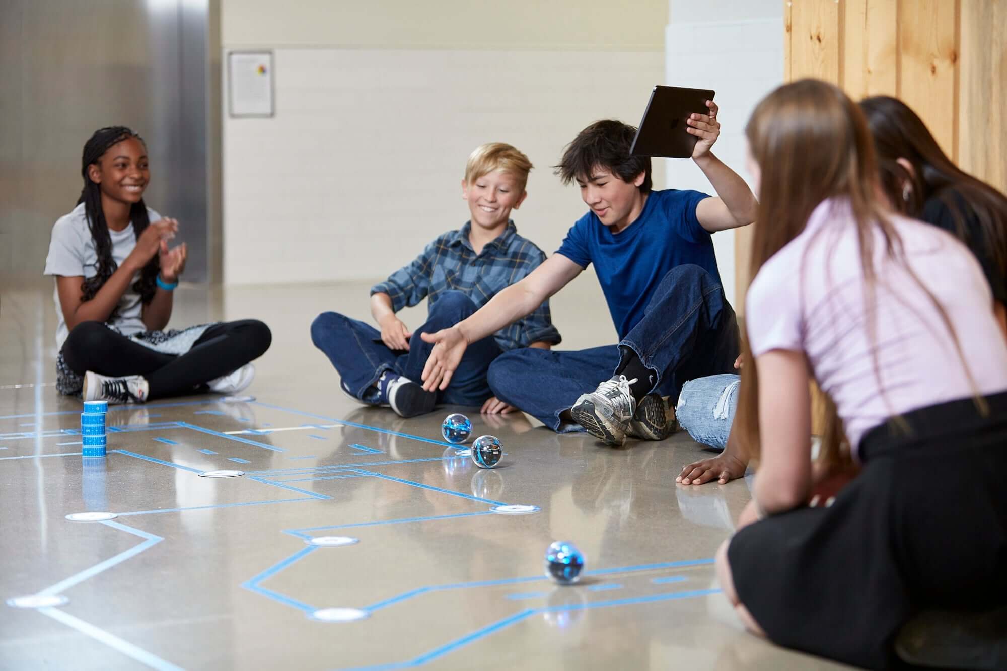 Students engaging with Sphero BOLT+ robots while coding on a floor grid in a classroom setting.