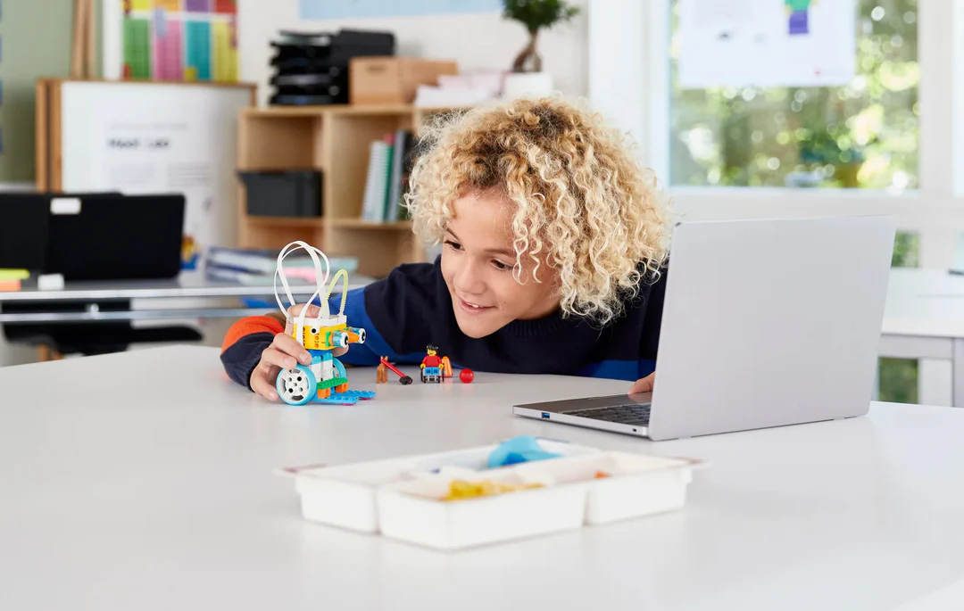 Child engaging with LEGO robotics kit while using a laptop, promoting STEM education and creativity.