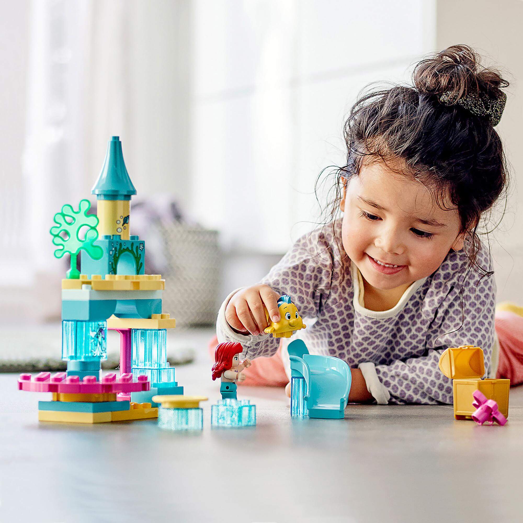 Child playing with LEGO® DUPLO Princess Ariel Undersea Castle set, featuring Ariel and Flounder figures for imaginative adventures.