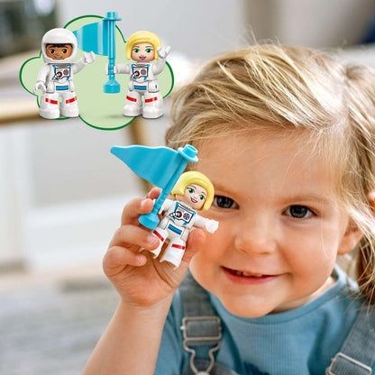 Toddler girl holding LEGO DUPLO astronaut figure with flag, excitedly engaging in space exploration play.