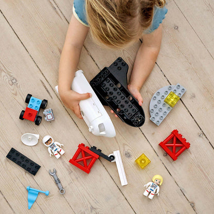 Child playing with LEGO® DUPLO Space Shuttle Mission set pieces on wooden floor, enhancing creativity and developmental skills.