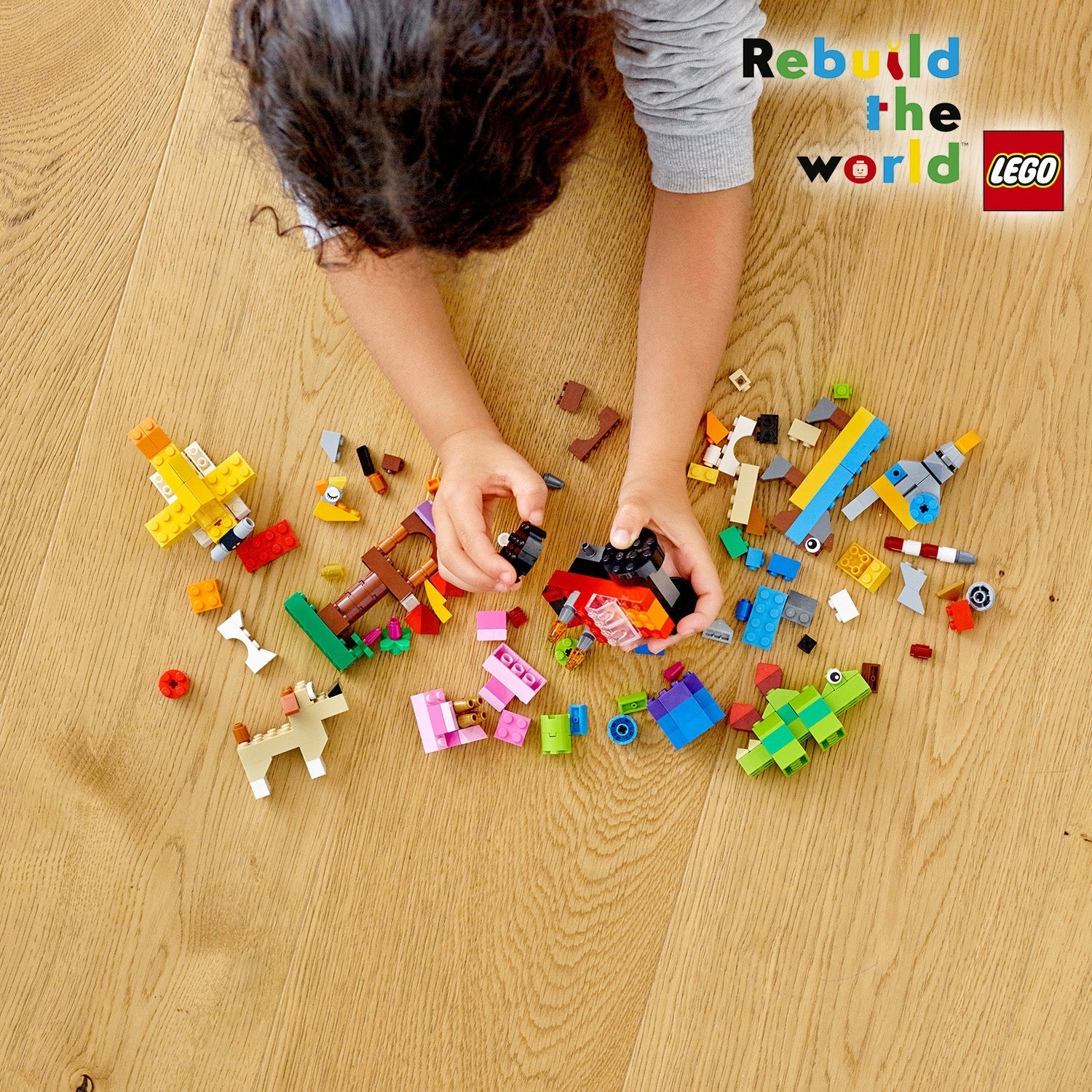 Child playing with LEGO® Classic Basic Brick Set 11002, surrounded by colorful building blocks on a wooden floor.