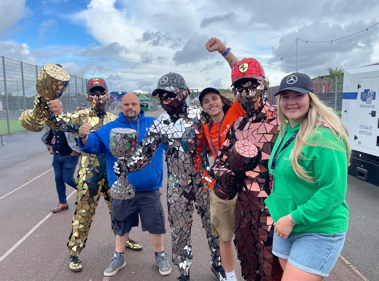 Group of fans in reflective suits posing at a sports event, celebrating with trophies in hand.