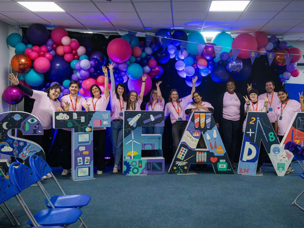 Group of educators celebrating at a STEAM event with colorful balloons and themed decorations.