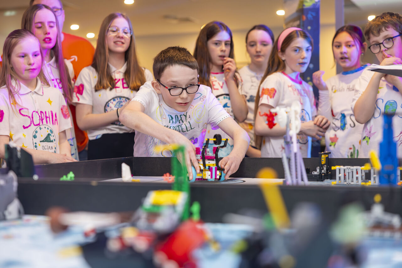 A group of children participating in a robotics class, with one boy focusing on building in the foreground.