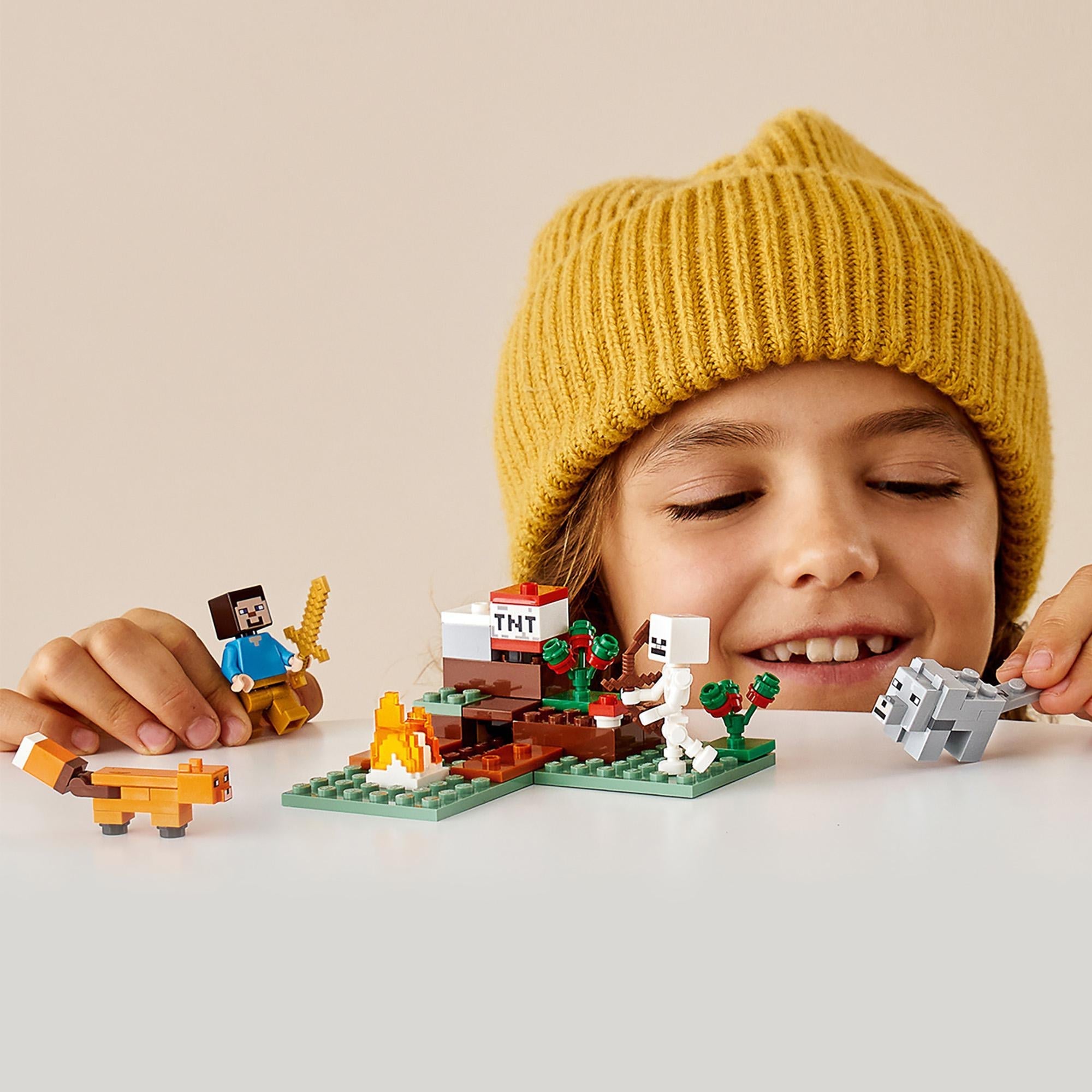 Child playing with LEGO® Minecraft The Taiga Adventure Set 21162 featuring characters like a fox and skeleton.