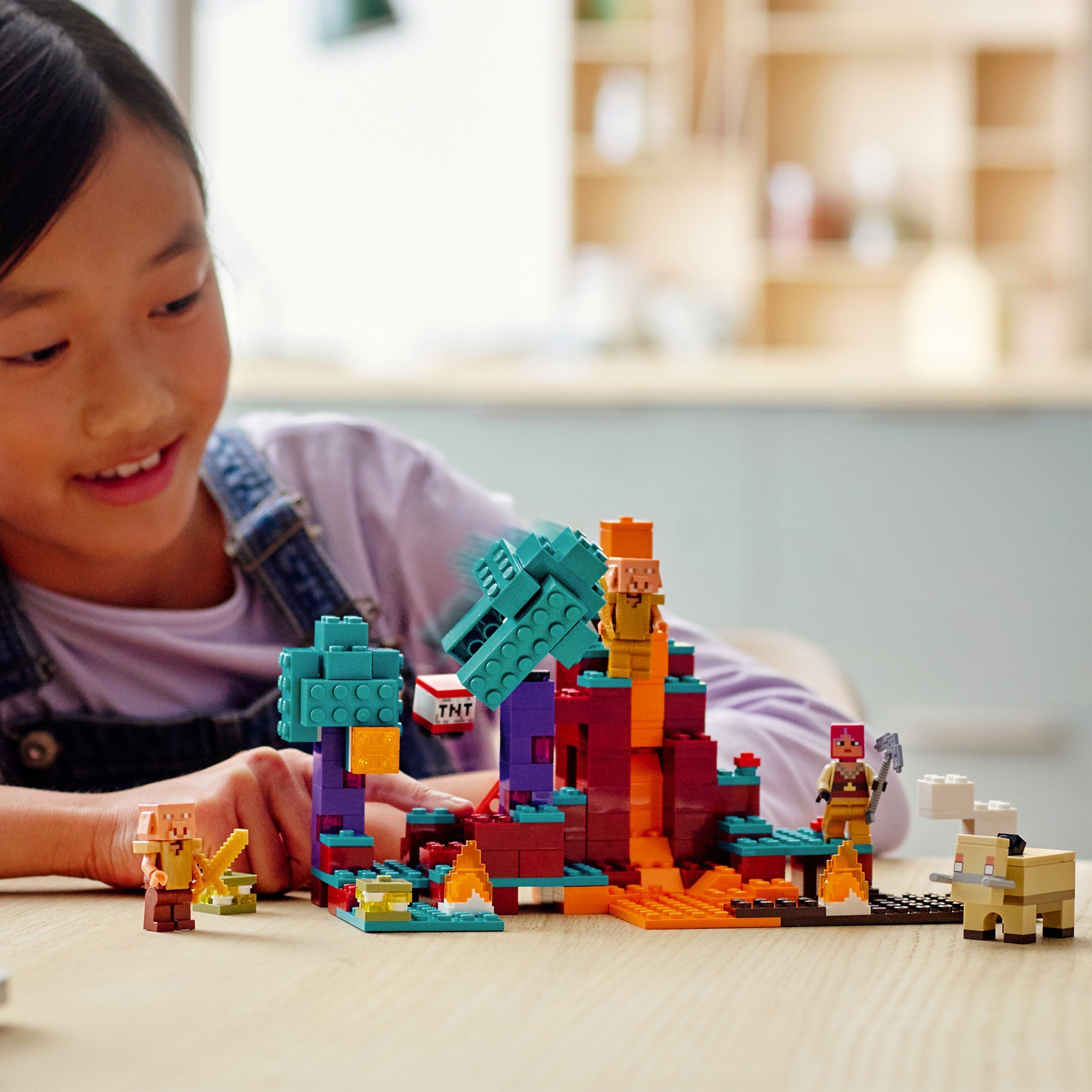Child playing with LEGO® Minecraft The Warped Forest set, featuring characters, lava flows, and vibrant trees.