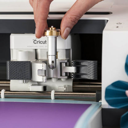 A hand attaching a scoring wheel to a Cricut Maker for crafting projects.