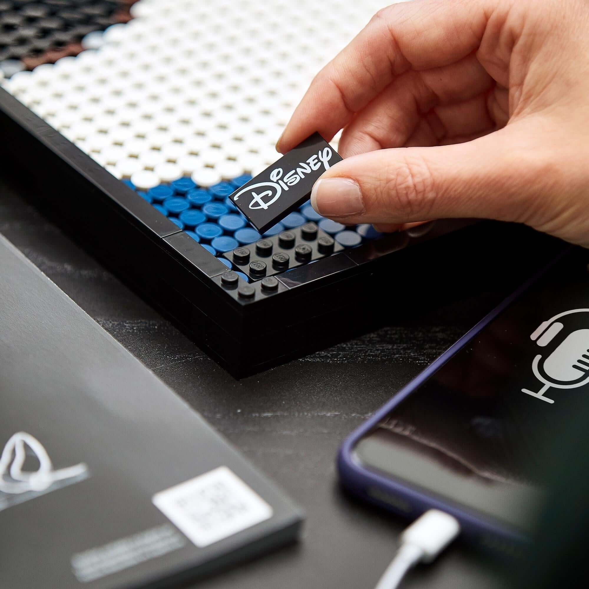 Hand placing a Disney LEGO® piece into a colorful mosaic during the Mickey Mouse wall art creation process.