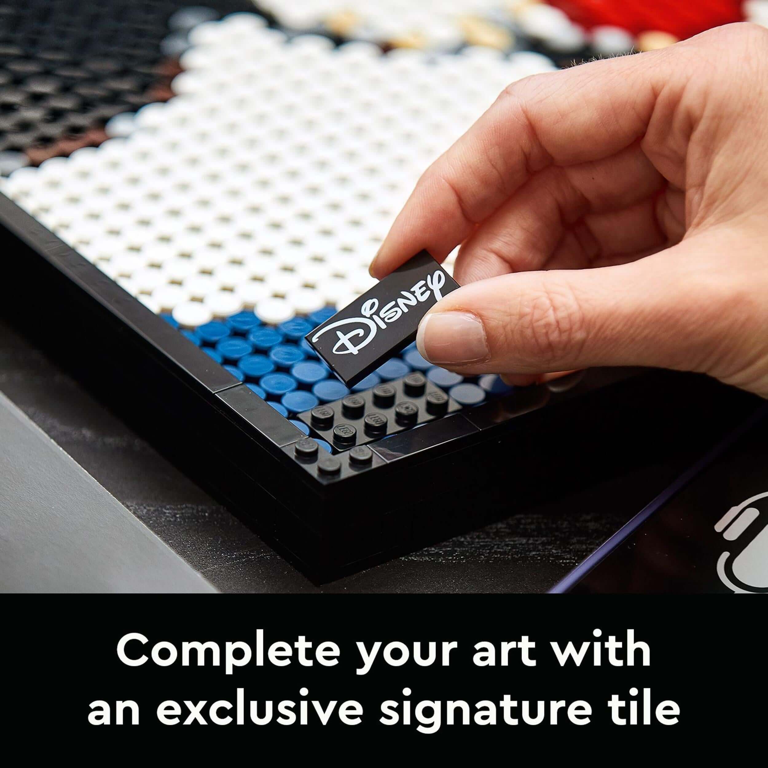 Hand placing a signature tile on LEGO® Disney Mickey Mouse art set 31202, showcasing creativity and craftsmanship.