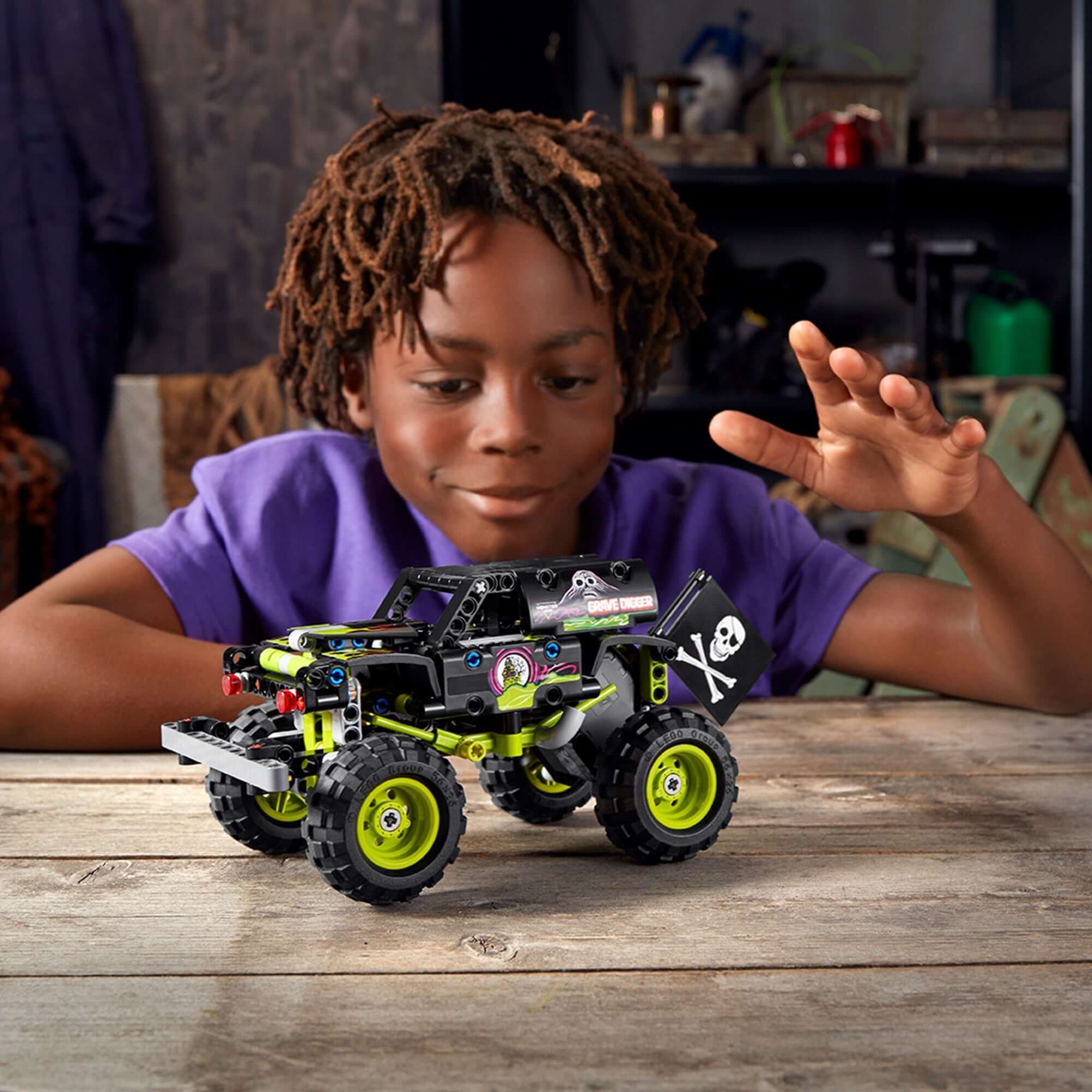 Child playing with LEGO Technic Monster Jam Grave Digger toy 42118 on a wooden table, showcasing creativity and fun.